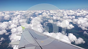 Footage of the airplane wing from the window which is flying over clouds in the blue sky