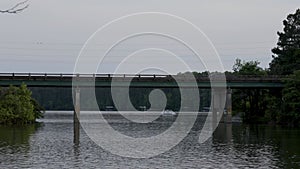 Footage of cars and trucks driving across a bridge over the rippling waters of Lake Acworth surrounded by lush green trees