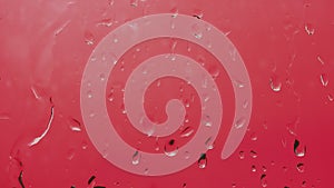 A footage of drops flow down the glass on a beautiful red background. Rain drops, thunderstorm background. Water splash