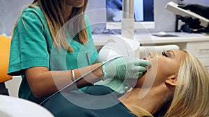 Footage of a female patient sitting in the dentists chair and a female dentist takes an x-ray shot of the patients teeth