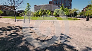 footage of gorgeous spring landscape at Miller Park with green trees and grass, people walking and office buildings, retail stores