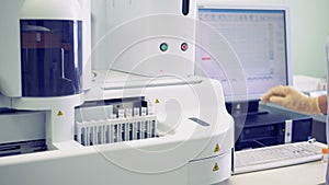 Footage of a laboratory testing machine with test tubes in it and lab assistant setting data on the computer