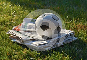 A football ball amongst sports newspapers on a green field. Symbol of the power of sports journalism to inform and inspire people