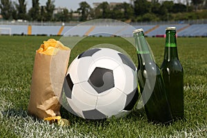 Football ball with beer and chips on green field grass in stadium