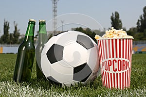 Football ball with beer and popcorn on green field grass in stadium
