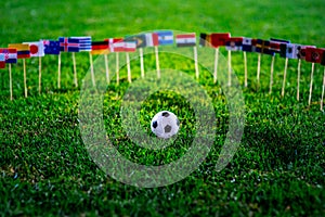 Football ball on green grass and all national flags of World Cup in Russia 2018