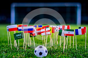 Football ball on green grass and all national flags of World Cup in Russia 2018