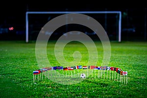 Football ball on green grass and all national flags of World Cup in Russia 2018