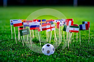 Football ball on green grass and all national flags of World Cup in Russia 2018