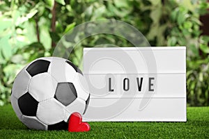 Football ball, lightbox with word Love and heart on green grass against blurred background