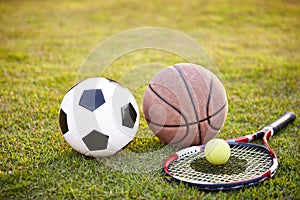 Football basketball and tennis ball and racket on grass