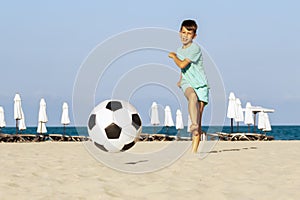 Football on beach. Boy soccer player kick ball in football match on sand. Summer holiday outdoor on sea shore