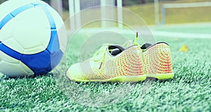 Football boots next to a football ball on the grass of the stadium