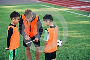 Football coach instruct teen football players. Young professional coach explains for kids the strategy of the game.