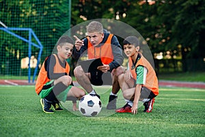 Football coach instruct teen football players. Young professional coach explains for kids the strategy of the game.