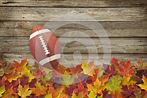 Football with fall leaves on rough wood top view