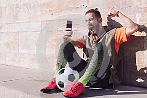 Football fan celebrating victory consulting phone