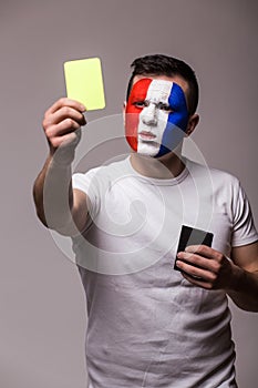 Football fan of France national football team show yellow card on camera on grey background.