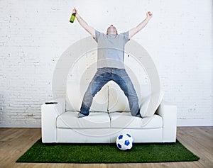 Football fan watching tv match on sofa with grass pitch carpet celebrating goal