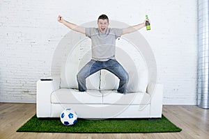 Football fan watching tv match on sofa with grass pitch carpet celebrating goal