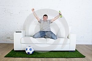 Football fan watching tv match on sofa with grass pitch carpet celebrating goal