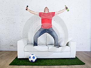 Football fan watching tv soccer celebrating goal in couch on grass carpet emulating stadium pitch