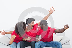 Football fans in red sitting on couch cheering