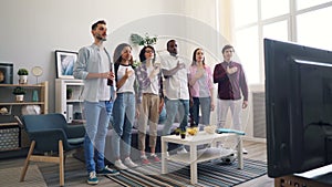 Football fans singing national anthem standing indoors watching match on TV