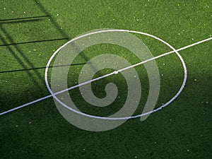 Football field markings. White central circle and line on a green background. Autumn leaves have fallen on the football field.