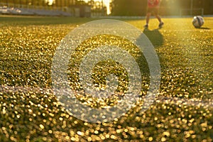 A football field in the sunlight with the player`s feet and the ball in the background