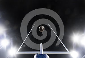 Football flying through the uprights of the field goal posts during a night football game