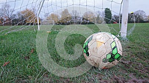 A football on the goal line of a muddy football pitch