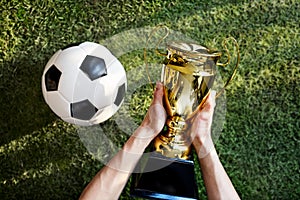 Football on ground next to man holding the winning trophy