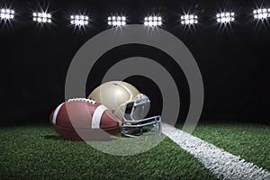 Football and helmet on grass field below stadium lights at night