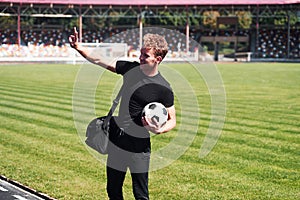 Football player on the field. Sportive young guy in black shirt and pants outdoors at daytime