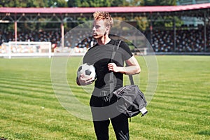 Football player on the field. Sportive young guy in black shirt and pants outdoors at daytime