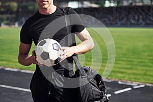 Football player on the field. Sportive young guy in black shirt and pants outdoors at daytime