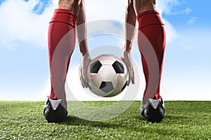 Football player in red socks and black shoes holding ball in his hands placing free kick or penalty