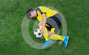 Football player in Yellow lying injured on the pitch.