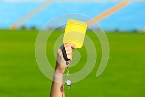 Football referee holding yellow card and whistle at stadium