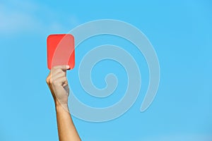 Football referee showing red card against blue sky