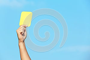 Football referee showing yellow card against blue sky