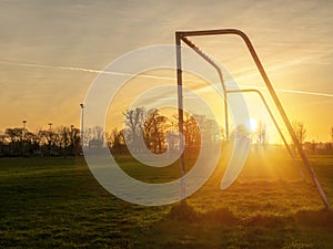 Football or soccer goal post on a green grass pitch in a park at sunset time. Nobody. Calm mood. Sun flare. Sport theme background