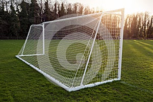 Football or soccer goal post on a training ground in a park at sunset. Warm color. Sun flare. Nobody. Outdoor activity. Calm