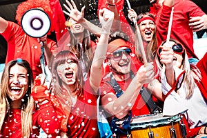 Football supporter fans cheering with confetti watching soccer match cup at stadium tribune - Young people group with red t-shirt photo