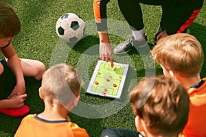 Football training. Soccer coach explaining game rules and strategy using tablet, map. Sports junior team sitting on