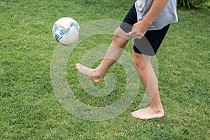 Footballer barefoot stuffs the ball on the green grass.