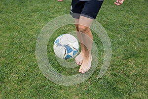 Footballer barefoot stuffs the ball on the green grass.