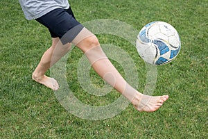 Footballer barefoot stuffs the ball on the green grass.