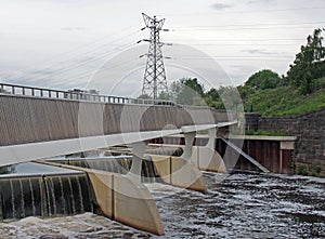 Footbridge crossing the flood alleviation weir on the river aire at knostrop leeds with electricity pylons in a rural industrial